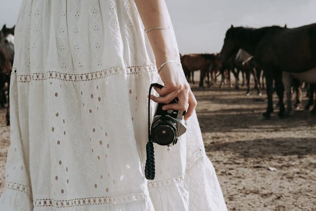 Woman in a white dress holding a camera, preparing to take high-quality photos of her horse for a sale listing.